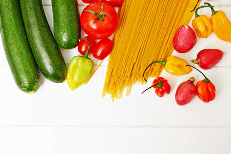 Raw spaghetti pasta with vegetables on white wooden tableの写真素材