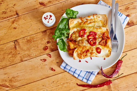 Enchiladas dish with red chili peppers on wooden table, top view