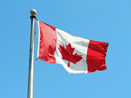 A Canadian flag waving in the wind against a blue sky