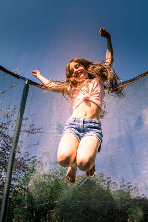young girl having fun in the sun flying and bouncing on a trampoline getting some excersiseの写真素材