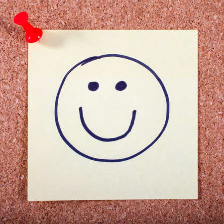 A Happy Face on a Memo Page pinned to a Noticeboard.の写真素材