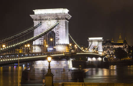 A night-time view of the historic Chain Bridge spanning over the River Danube in Budapest, Hungary.  St. Stephenâs Basilica can be seen in the distance.の写真素材