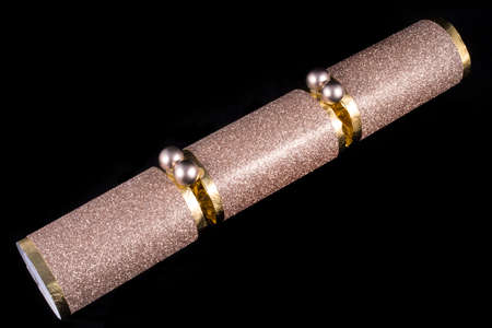 A studio shot of a Christmas Cracker or otherwise known as a Bon Bon.  A cracker consists of a cardboard tube wrapped in a decorated twist of paper with a gift in the central chamber.の写真素材
