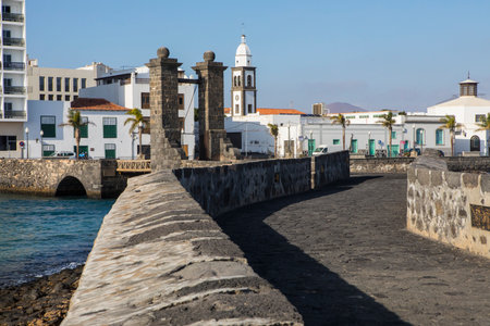 The drawbridge of Castillo de San Gabriel on the waterfront of Arrecife - the capital of the volcanic island of Lanzarote in Spain.  The tower of Iglesia de San Gines is in the background.のeditorial素材