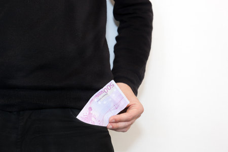 Young businessman standing with money in pocket against isolated white background