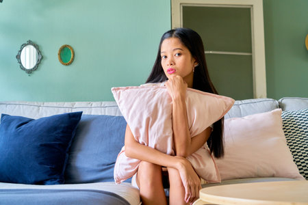 Beautiful woman posing - sitting in sofa, thinking and looking at cameraの写真素材