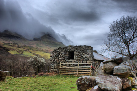 a disused barn in front of a moody sky over a mountainのeditorial素材
