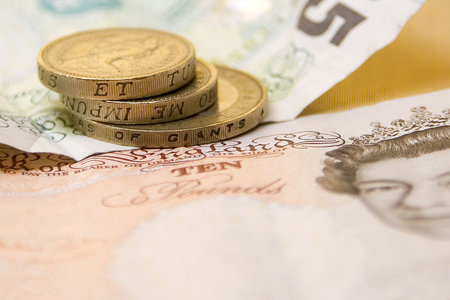 A five and ten pound note sit on a gold backdrop with a few pound coins.の写真素材