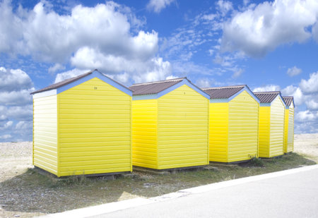 Four yellow beach huts on teh edge of a sandy beach.の写真素材