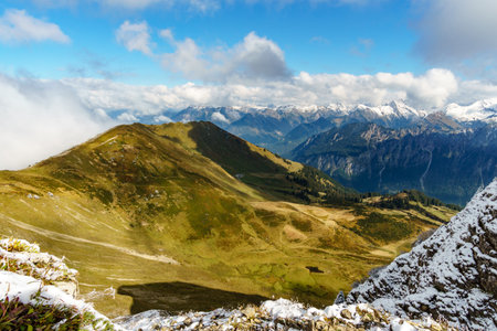 View of beautiful landscape in the Alps with fresh green meadows and snowcapped mountain tops in the background on a sunny day with blue sky and clouds in springtime.の写真素材