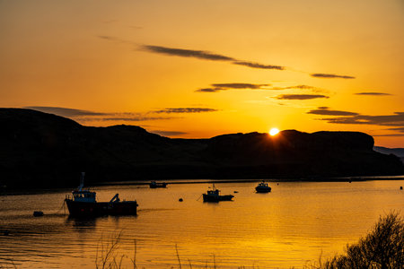 Boats in Portree bay during sunrise with purple and orange colors with hills on both sides on the Isle of Skyeの写真素材