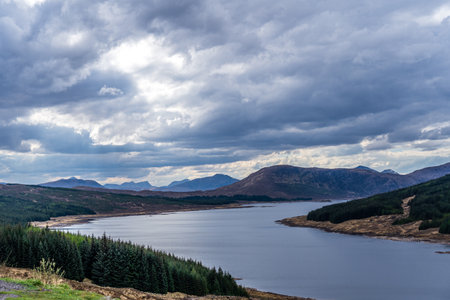 Beautiful layers of color of rural Isle of Skye landscape on an overcast day. From loch shore at low tide to the rolling hills of the countryside and the Cuillin mountain rangeの写真素材