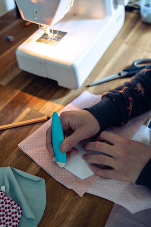 a woman draws paper details with chalk on a black fabric for sewing protective masks at home, top...