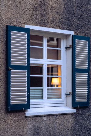A coiled compact fluorescent light bulb glowing in dark. The bulb is inside a metal wall lantern attached to the brick wall of the exterior of a house. Electricity, power, energy consumption concept.の写真素材
