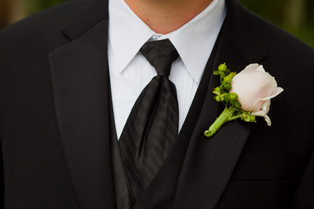 Groom wearing a boutonniere consisting of a rose and hypericumat a wedding.