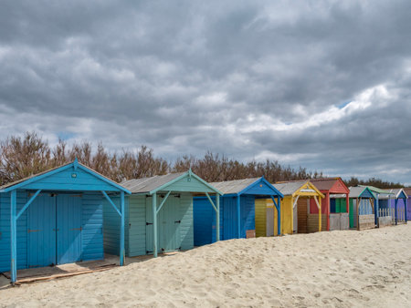 A row of colorful wooden beach huts on a sandy beach in the South of England on a cloudy dayの写真素材