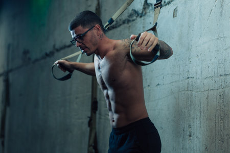 Young strong man in gym doing suspended exercises with straps in the gym
