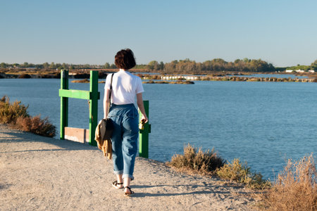 A young woman from behind looking the landscape on the bank of a small streamの写真素材