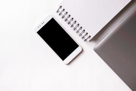 Close laptop on a white background next to a mobile phone and a ring notebook.の写真素材