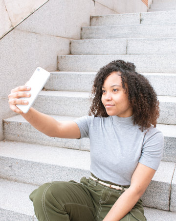 A woman with curly hair taking a selfie smiling while sitting on a staircase.の写真素材
