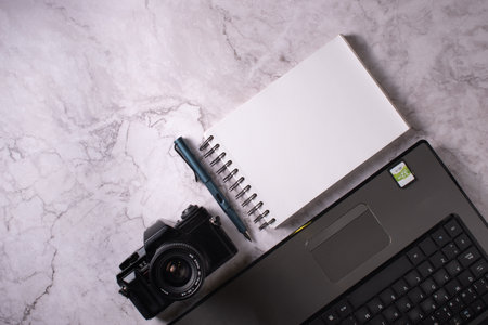 Photographer's work equipment consisting of a camera, a laptop and a notebook on a marble table.の写真素材