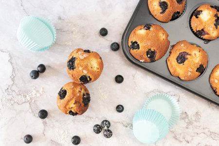 Top view of blueberry muffins with several loose blueberries and a little flour on a marble table.の写真素材