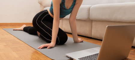 Young attractive woman doing yoga while watching online classes on her laptopの写真素材