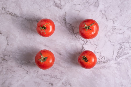 Four tomatoes with drops of water on a marble background.の写真素材