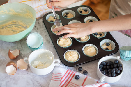Unrecognizable person preparing a batch of blueberry muffins in the kitchen.の写真素材