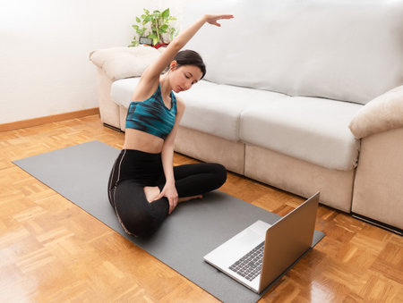 Woman stretching at home while looking at her laptop.の写真素材