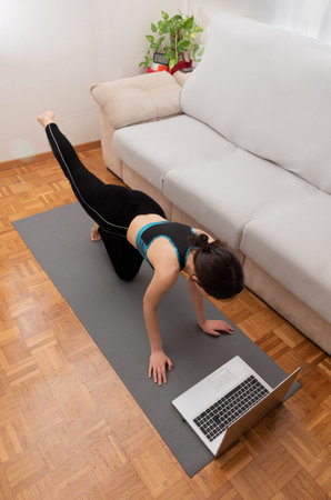 Unrecognizable young woman exercising at home while taking online classes. Vertical.の写真素材