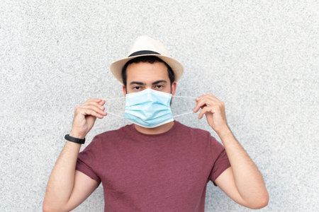Young man with hat putting on blue maskの写真素材
