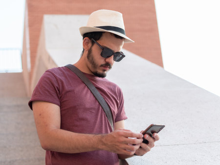 Man using his smartphone while wearing a hat and glasses.の写真素材