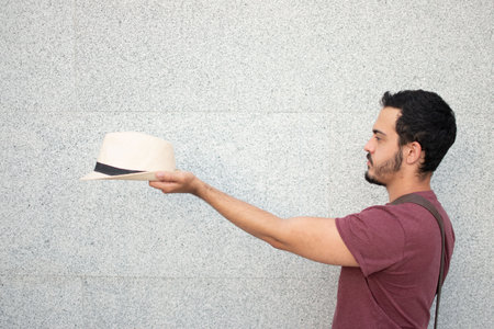 Young man sideways while holding a hat with his arm outstretched.の写真素材