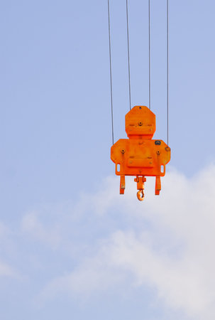 Orange heavy lift crane hook against a blue skyの写真素材