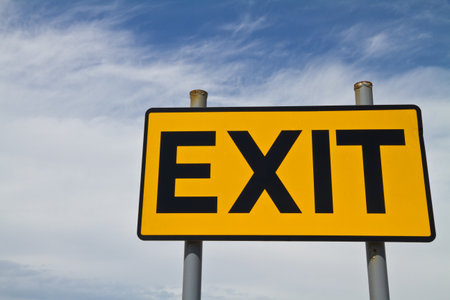 Yellow and Black Exit Sign against a cloudy and blue  skyの写真素材