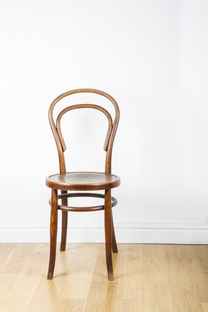 A single antique wooden chair, on a polished pine floor against a white wallの写真素材