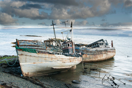 Three derelict fishing trawlers hauled up and rotting in a sea estuaryの写真素材