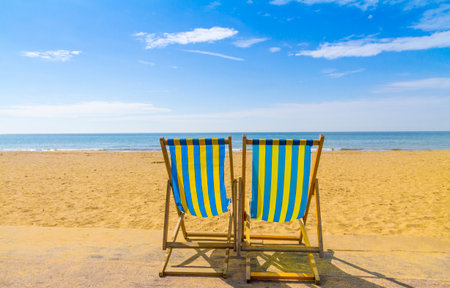 Two blue and yellow deckchairs facing the sea across golden sand on a bright sunny day, Bournemouth,...
