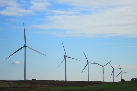 Windmill park producing substainable energi on green field with blue sky and clouds