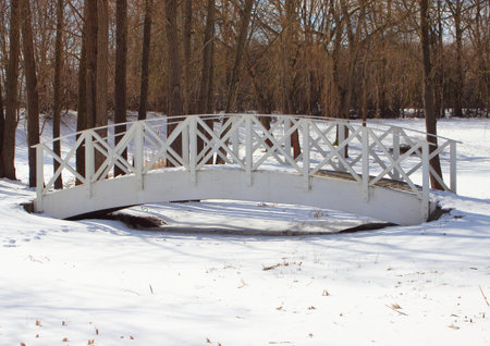 Wooden white bridge over snowy frozen waterの写真素材