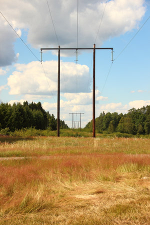 Wooden electrical tower in grass field with cloudsの写真素材