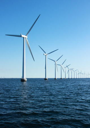 Vertical perspective line of ocean windmills with dark water and sky