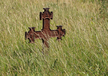 Isolated Rusty Iron Cross at Ancient Graveyard in Grass Fieldの写真素材