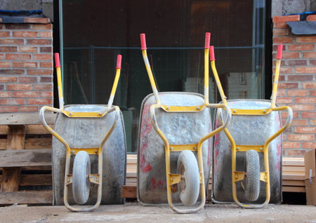 Three Metal Wheelbarrows with Red Handles at Construction Site Closeupの写真素材