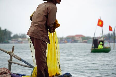 vietnamese fisherman on small boat fishing with fishnet