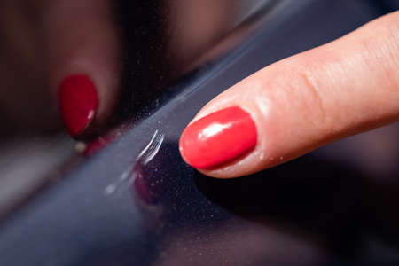 A woman shows scratches in a car paint.