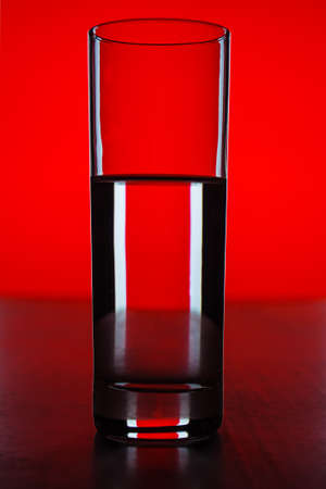Glass with water with red background - photo of an objectの写真素材