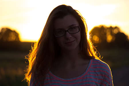 Beautiful teenager girl with glasses in the light of sunsetの写真素材