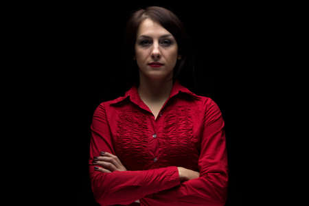 Photo of serious woman in red shirt with arms crossed on black backgroundの写真素材